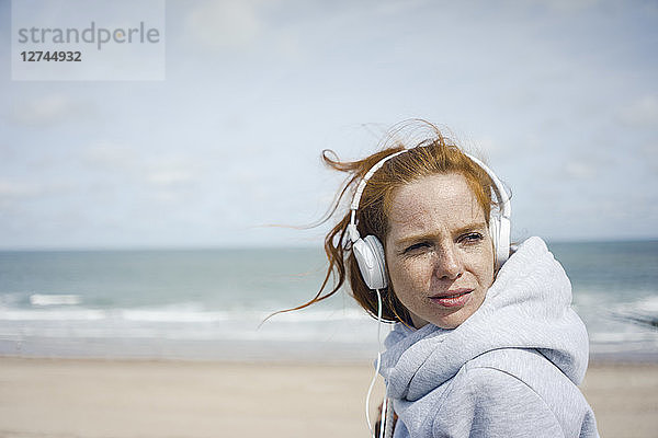 Redheaded woman relaxing at the beach  listening music with headphones