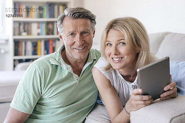 Portrait of smiling mature couple at home with tablet