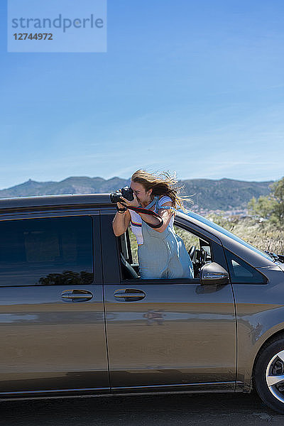 Happy woman leaning out of car window  taking pictures