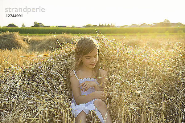 Little girl sitting on straw of havested field