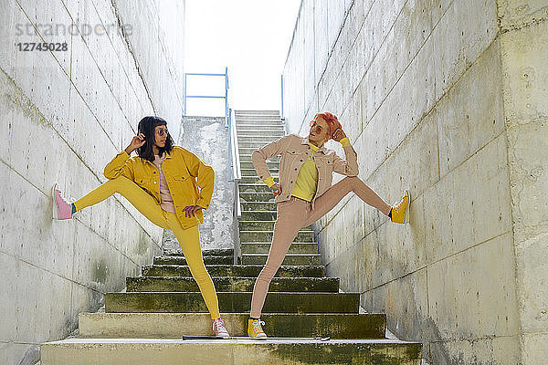 Two alternative friends posing on steps  wearing yellow and pink jeans clothes