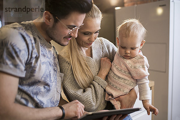 Young parents using tablet at home with their baby girl