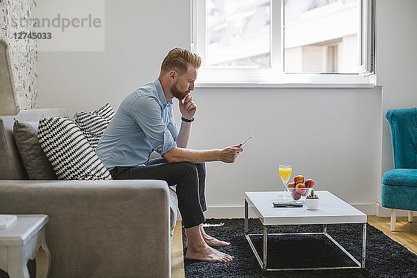 Businessman sitting on couch at his living room looking at smartphone