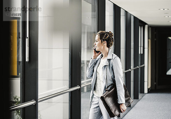 Businesswoman on cell phone looking out of window in office passageway