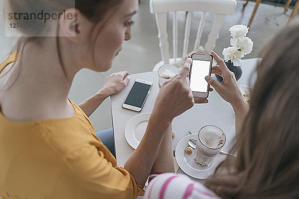 Two girlfriends meeting in a coffee shop  using smartphone
