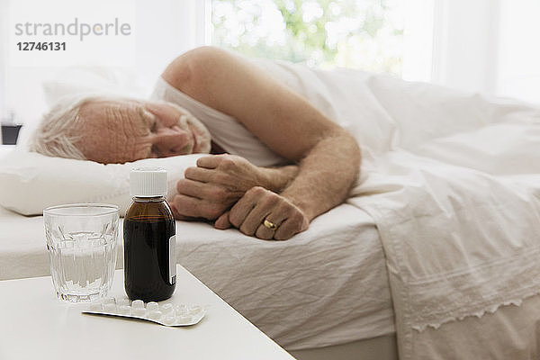 Tired senior man sleeping next to night stand with cough syrup and medicine