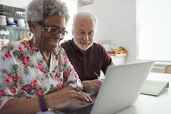 Senior couple paying bills at laptop in kitchen