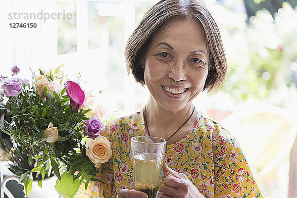 Portrait smiling  confident senior woman drinking tea next to flower bouquet