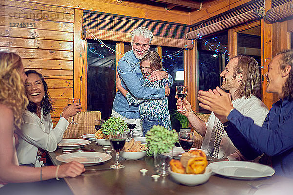 Friends clapping for affectionate couple hugging at dinner table