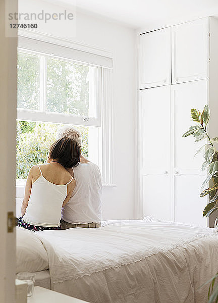 Serene senior couple sitting on bed and looking out window