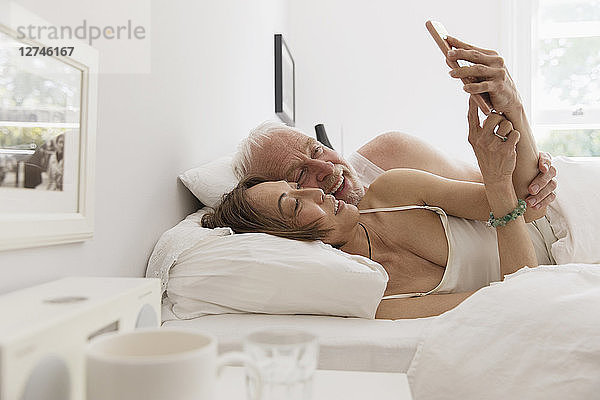 Affectionate senior couple using smart phone in bed