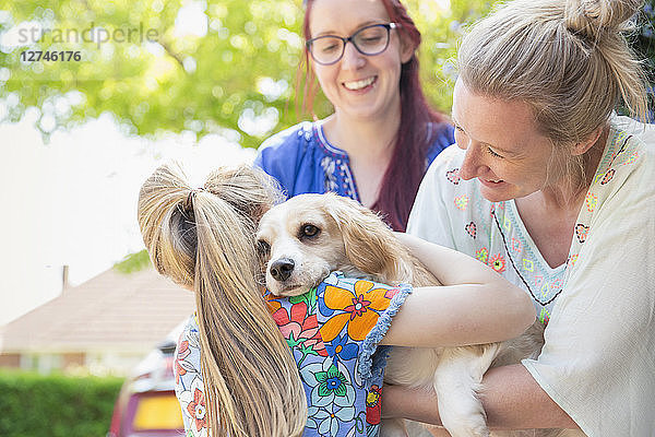 Lesbian couple and daughter hugging cute dog