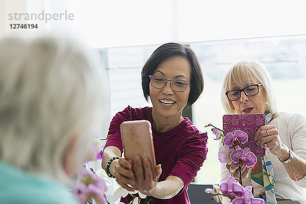 Active senior women with camera phone photographing orchids in flower arranging class