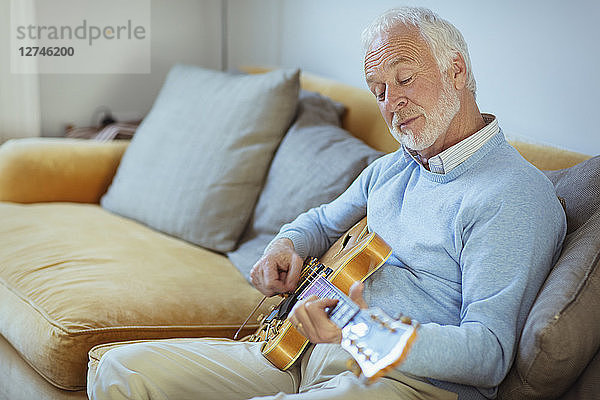 Active senior man playing guitar on living room sofa
