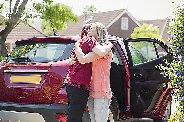 Affectionate lesbian couple hugging by car in sunny driveway