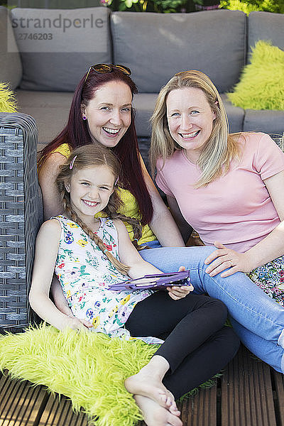 Portrait happy lesbian couple and daughter relaxing on patio