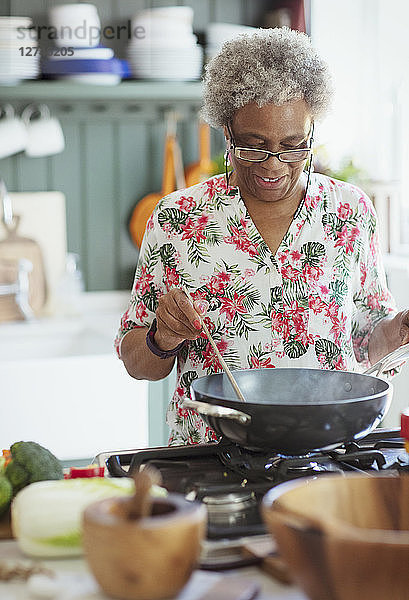 Active senior woman cooking at stove in kitchen