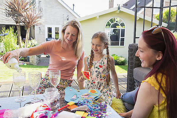 Lesbian couple enjoying white wine and doing craft project with daughter on patio