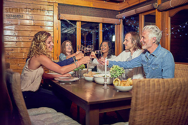 Friends toasting red wine glasses  enjoying dinner at cabin dining room table
