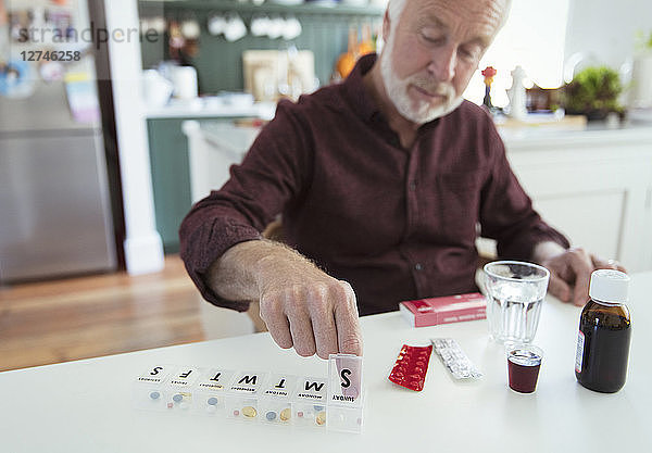 Senior man organizing pill box at kitchen table