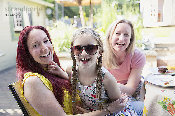 Portrait happy lesbian couple and daughter with sunglasses on patio