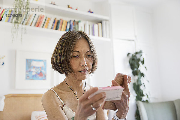 Senior woman with smart phone looking at box of medicine
