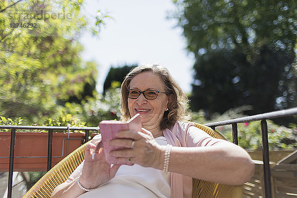 Happy senior woman using smart phone on sunny patio
