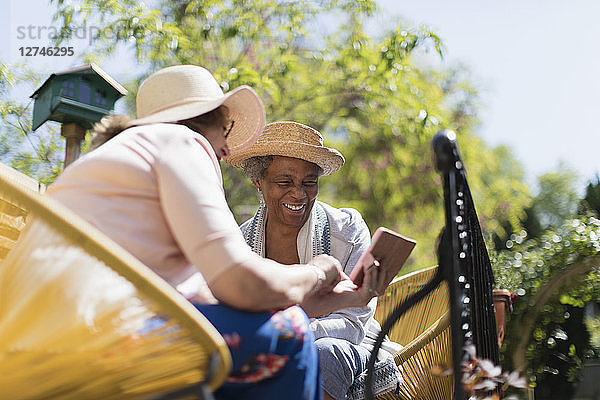 Senior women friends using smart phone on sunny patio