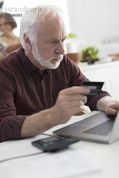 Focused senior man with credit card paying bills at laptop