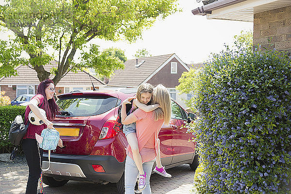 Affectionate lesbian couple and daughter at car in sunny driveway