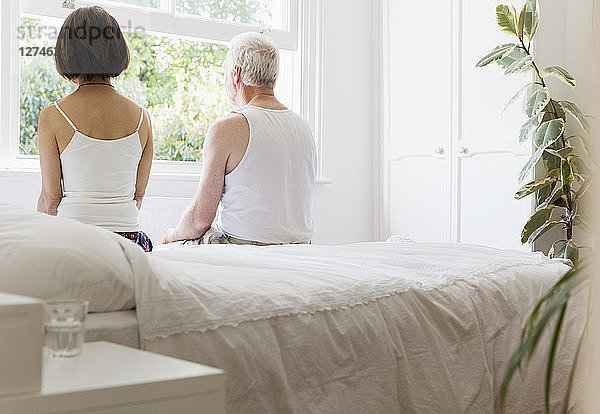 Thoughtful senior couple sitting on bed looking out window