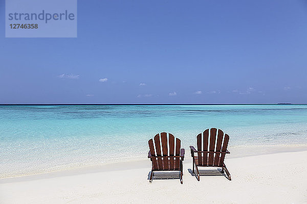 Zwei Adirondack-Stühle am sonnigen  ruhigen Strand mit Blick auf den blauen Ozean  Malediven  Indischer Ozean