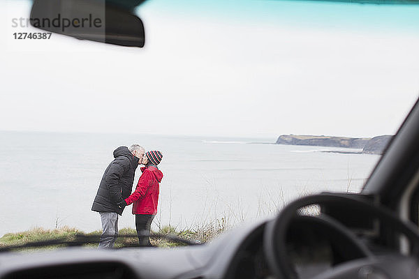 Zärtliches Paar küsst sich außerhalb des Wohnmobils auf einer Klippe mit Blick auf das Meer