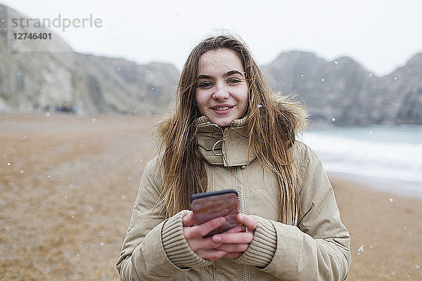 Porträt lächelnd Teenager-Mädchen SMS mit Smartphone auf verschneiten Winter Strand