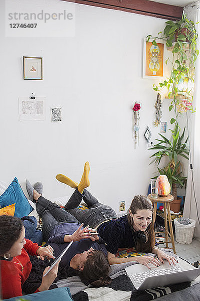 Junge befreundete Frauen  die auf dem Bett einen Laptop und ein digitales Tablet benutzen
