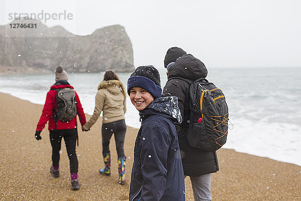 Porträt glücklicher Junge  der mit seiner Familie am verschneiten Wintermeerstrand spazieren geht