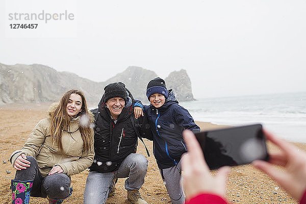 Glückliche Familie posiert für ein Foto am verschneiten Winterstrand