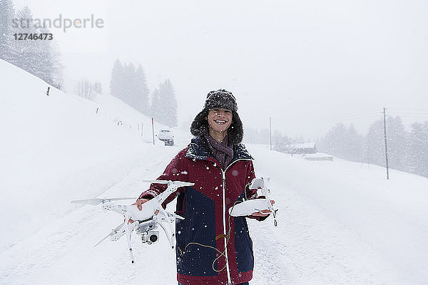 Porträt lächelnder Jugendlicher mit Drohne in verschneiter Landschaft