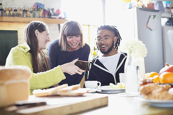 Junge Mitbewohner benutzen ihr Smartphone am Frühstückstisch in der Wohnung