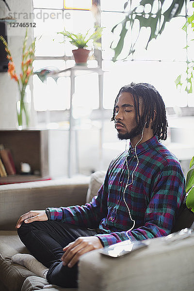 Gelassener junger Mann meditiert mit Kopfhörern im Sessel