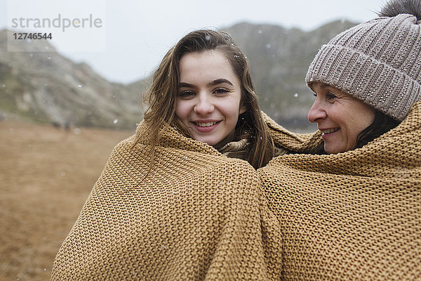 Portrait sorglose Mutter und Tochter in eine Decke eingewickelt am verschneiten Winterstrand