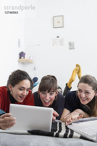 Junge Frauen  die auf dem Bett abhängen und ein digitales Tablet benutzen