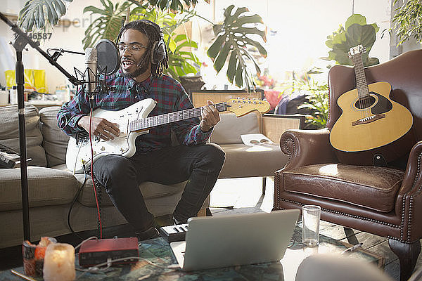 Junger männlicher Musiker nimmt Musik auf  spielt Gitarre und singt in ein Mikrofon in einer Wohnung