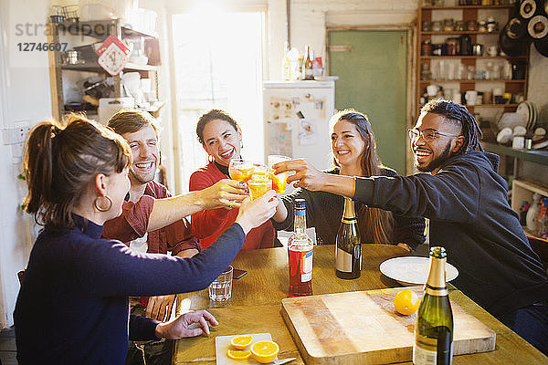 Fröhliche junge Erwachsene  die am Küchentisch in der Wohnung mit Cocktails anstoßen