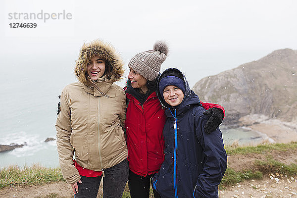 Porträt einer glücklichen Familie in warmer Kleidung  die auf einer Klippe mit Blick auf das Meer steht