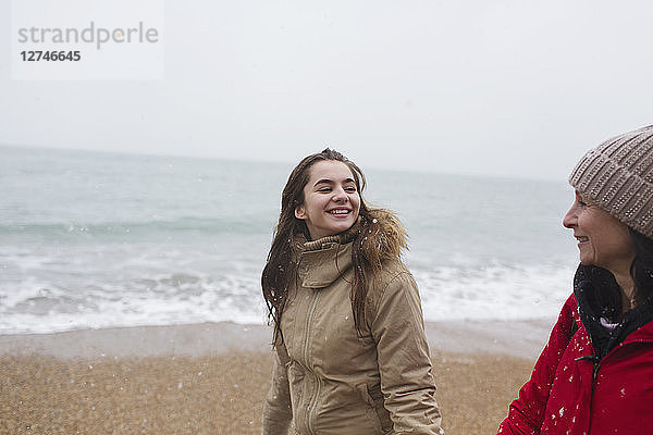 Mutter und Tochter in warmer Kleidung spazieren am winterlichen Meeresstrand