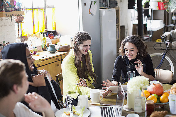 Junge Mitbewohner  die am Frühstückstisch in der Wohnung ein digitales Tablet und einen Laptop benutzen
