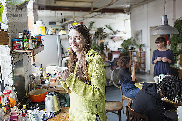 Lächelnde junge Frau beim Kaffeetrinken mit Mitbewohnern in der Wohnküche