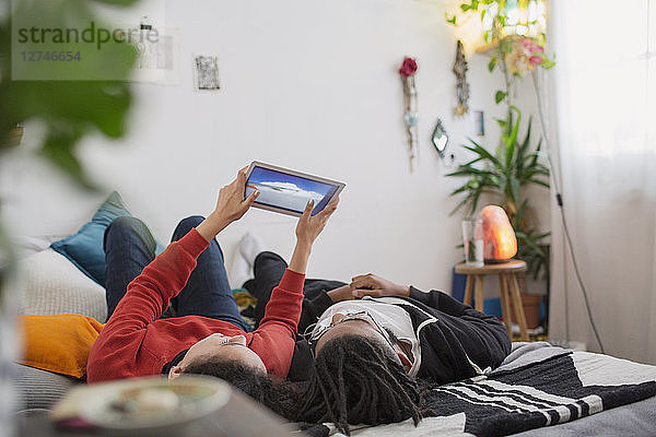 Junges Paar  das sich auf dem Bett mit einem digitalen Tablet entspannt