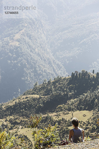 Weibliche Wanderin ruht sich aus und genießt die Aussicht auf die sonnigen grünen Ausläufer  Supi Bageshwar  Uttarakhand  Indischer Himalaya